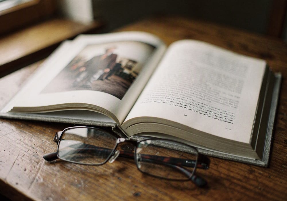 Aufgeschlagenes Buch mit Foto und Text, daneben eine Lesebrille